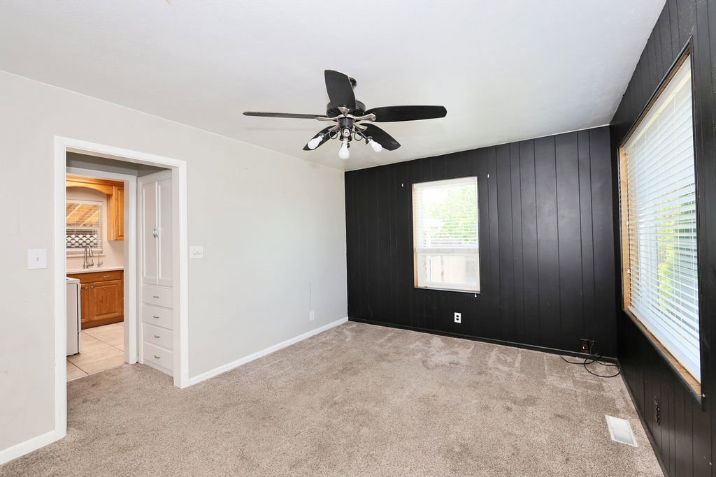 Carpeted room featuring a ceiling fan, a black accent wall with vertical paneling, and two windows with blinds