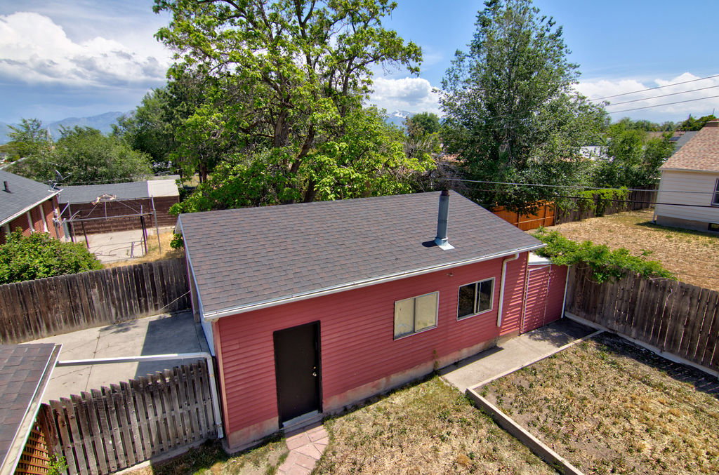 Detached red structure featuring a dark roof, a single dark entry door, two windows, and a metal chimney