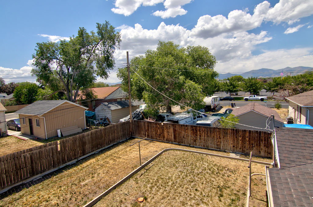 Expansive fenced backyard featuring a detached accessory structure with a dark shingle roof, mature perimeter trees, and a mountain backdrop