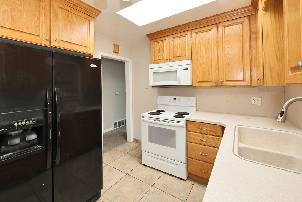 Kitchen featuring wood cabinetry, solid surface countertops, a ceramic tile floor, and a double basin sink with a pull-down faucet