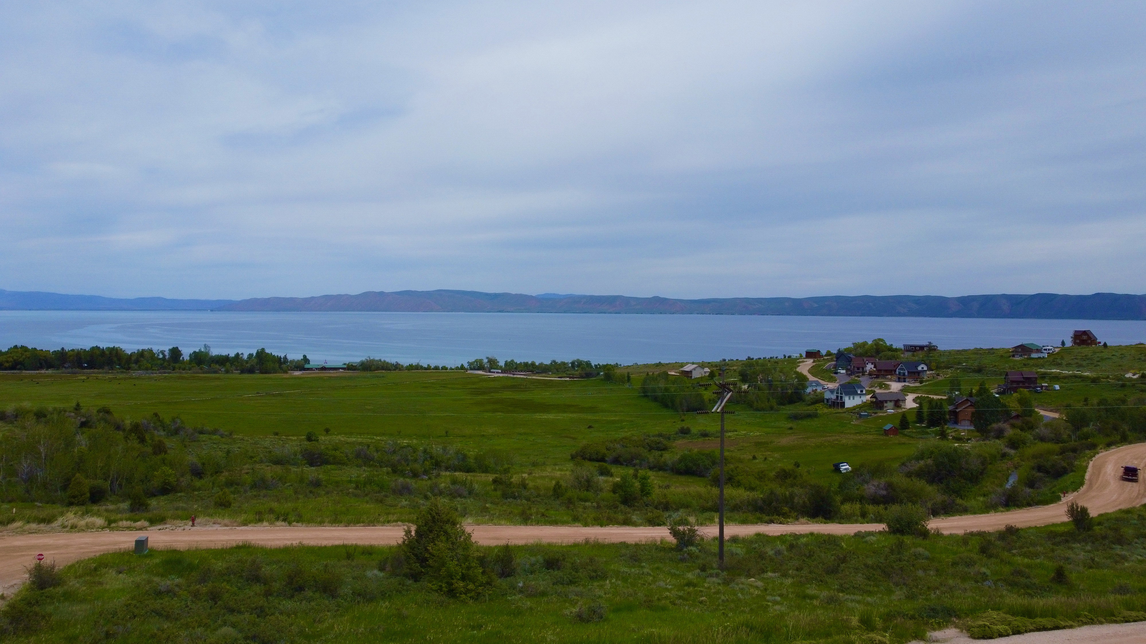 Expansive green landscape featuring a body of water, distant hills, and scattered residences