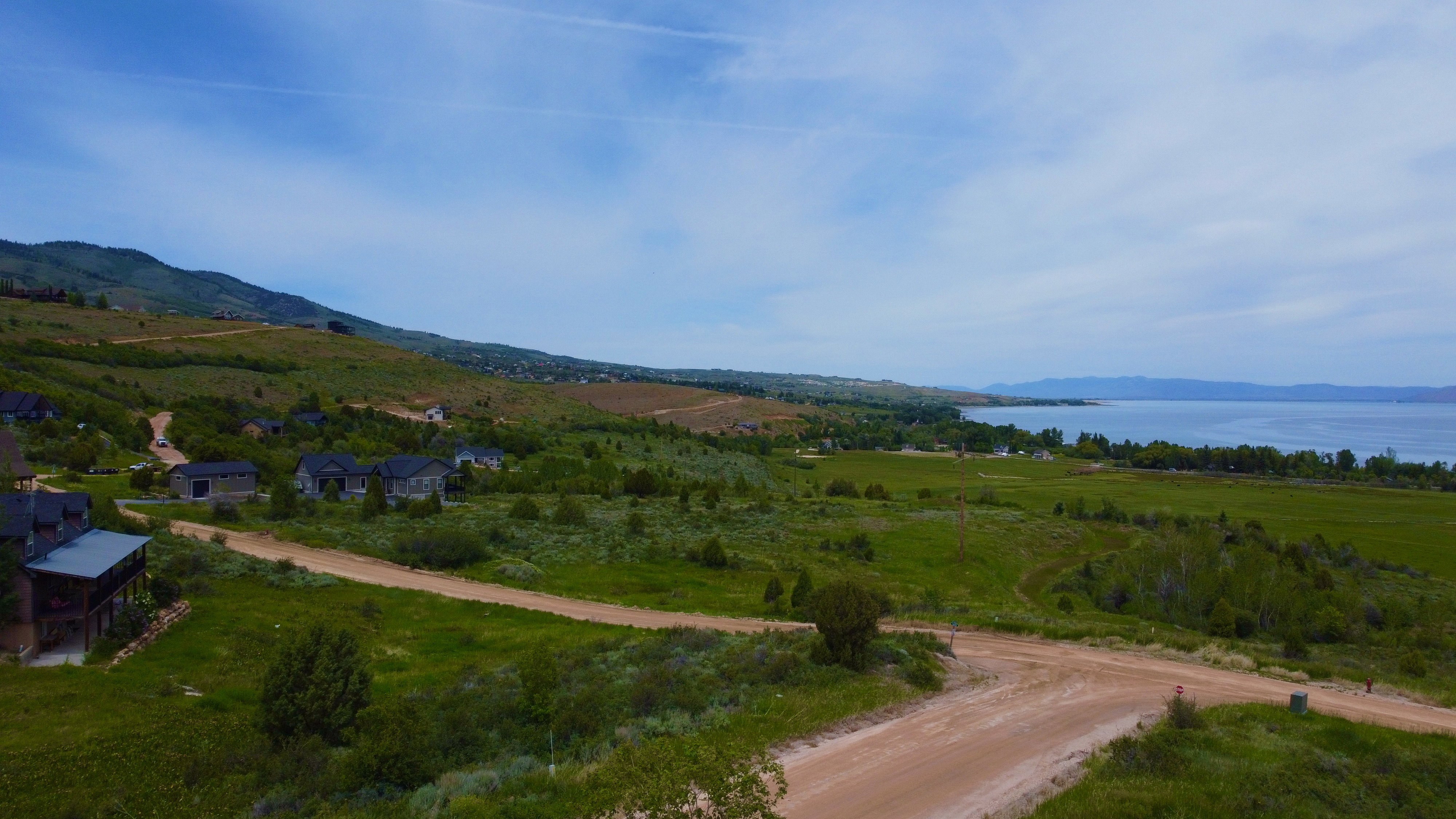 Expansive landscape featuring rolling green hills, a large body of water, and distant mountains under a blue sky