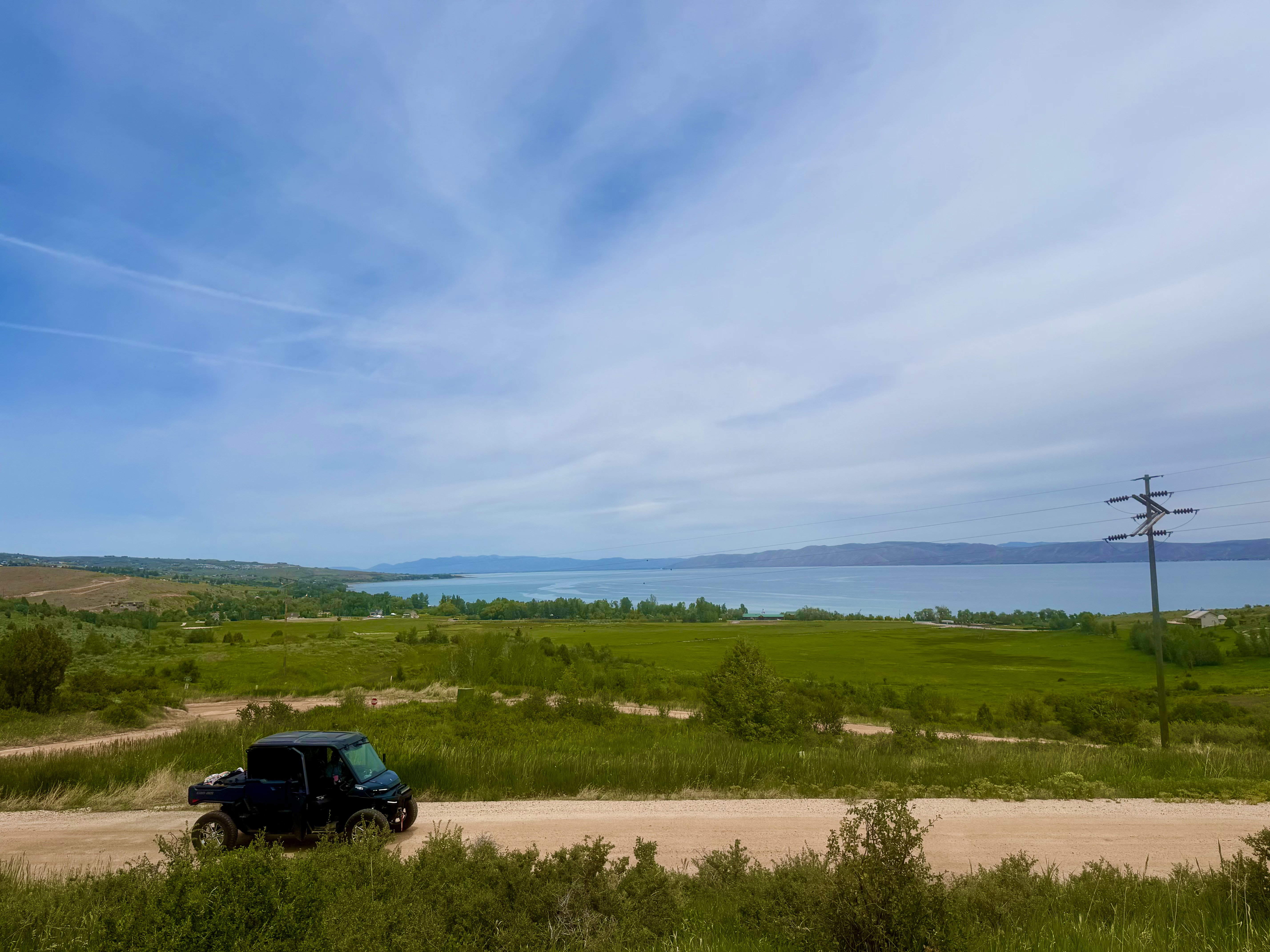 Expansive natural landscape featuring a prominent body of water, rolling green hills, and a clear sky overhead