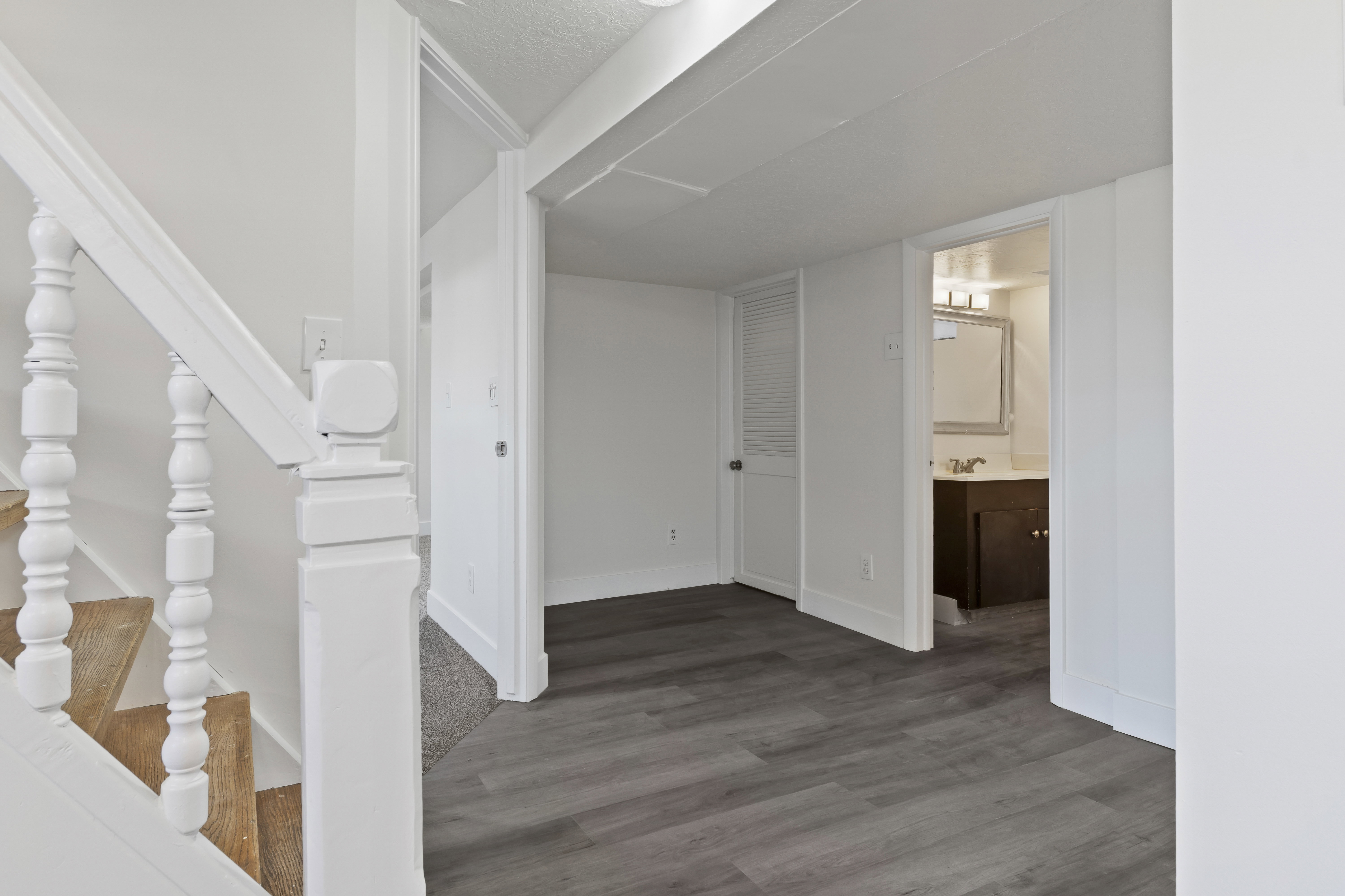 Interior hallway featuring wood-finish flooring, white trim, and a white staircase with turned balusters