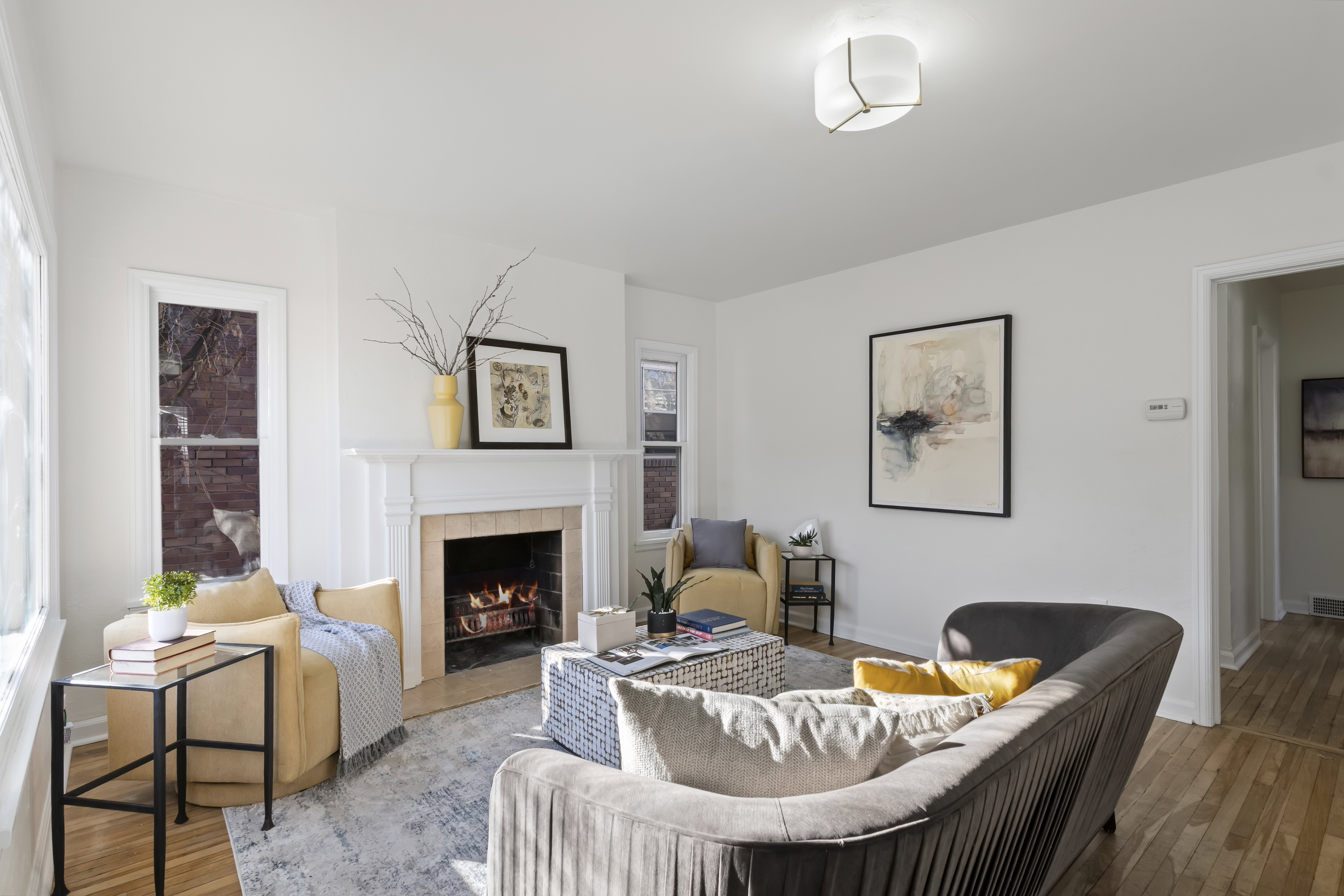 Living area featuring a classic white mantel fireplace with a light-colored tile surround, hardwood flooring, and abundant natural light from multiple windows