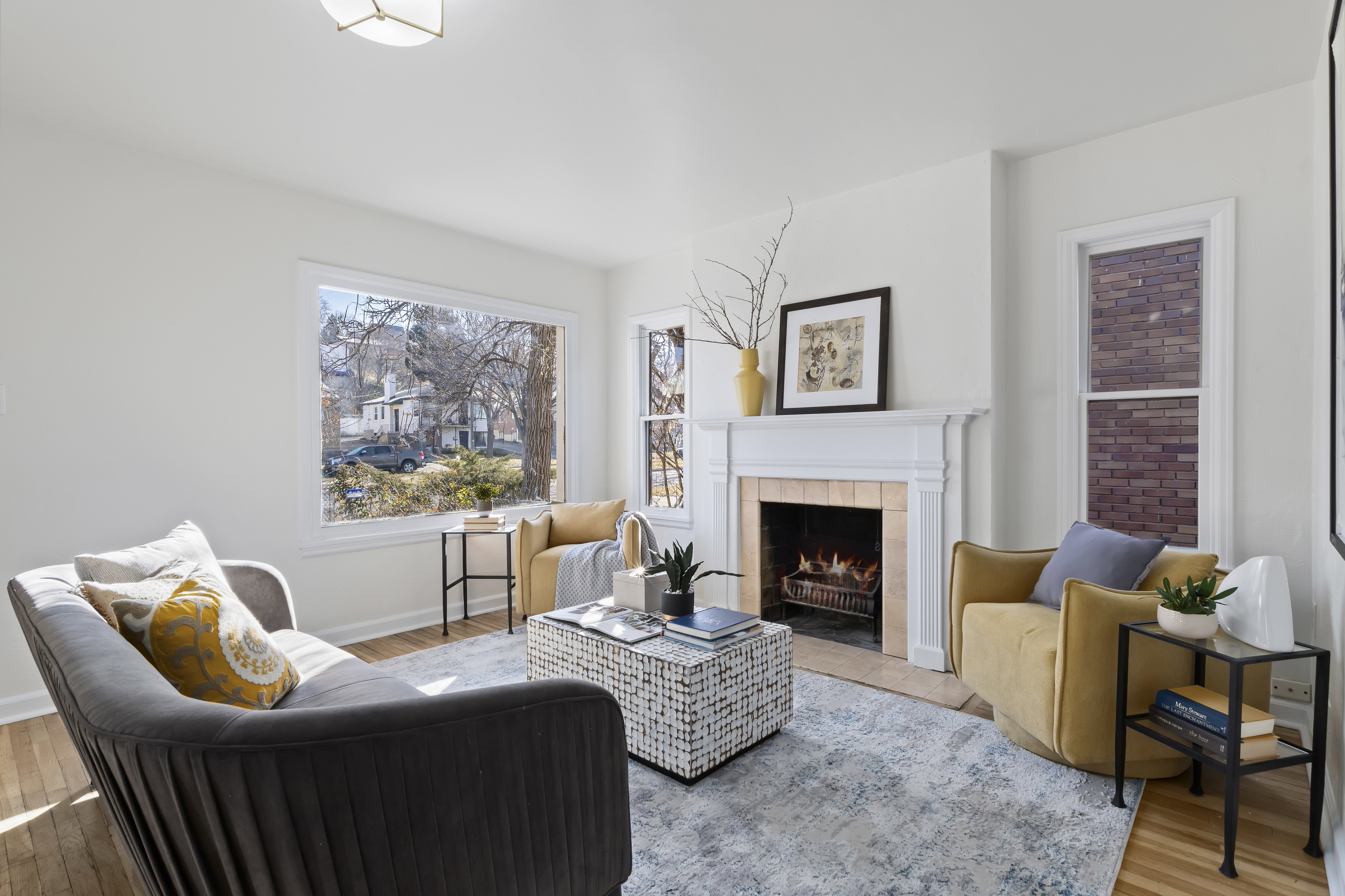 Bright living area featuring wood-finish flooring, a decorative fireplace with a white mantel, and large windows providing abundant natural light