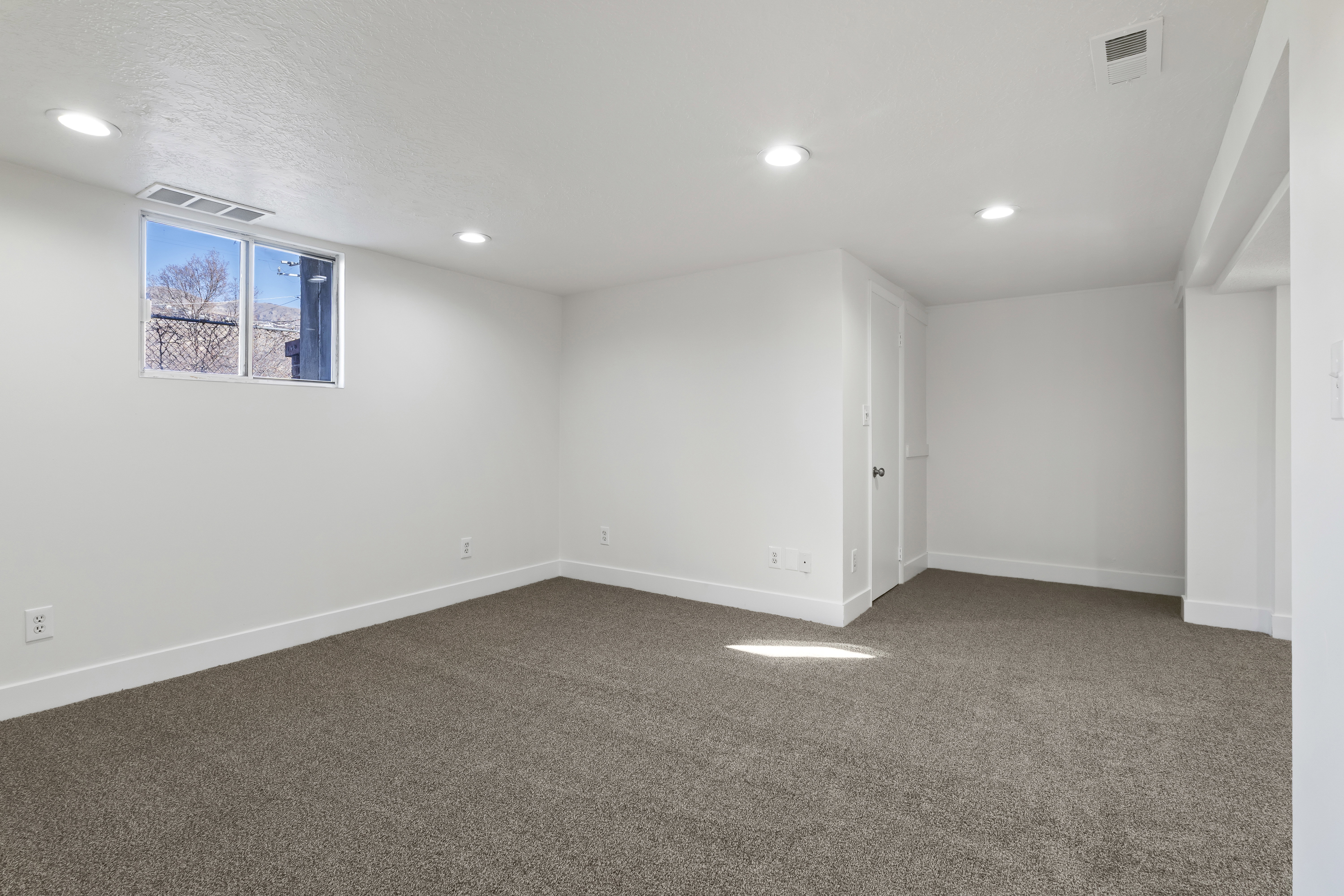 Spacious room featuring new carpeting, recessed lighting, a white trim package, and a window providing exterior visibility