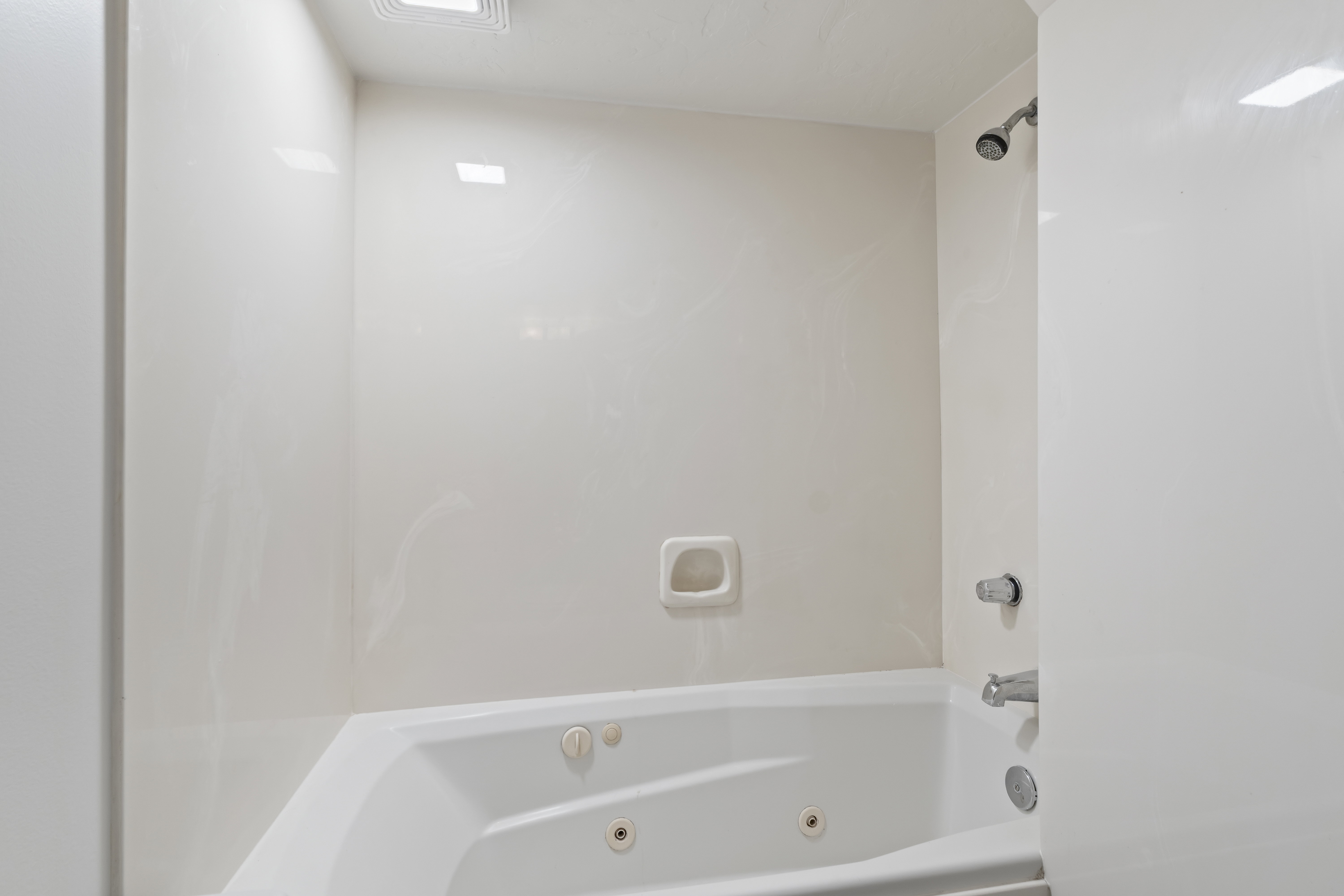 Bathtub and shower combination featuring an integrated corner jetted tub, a wall-mounted showerhead, and chrome fixtures