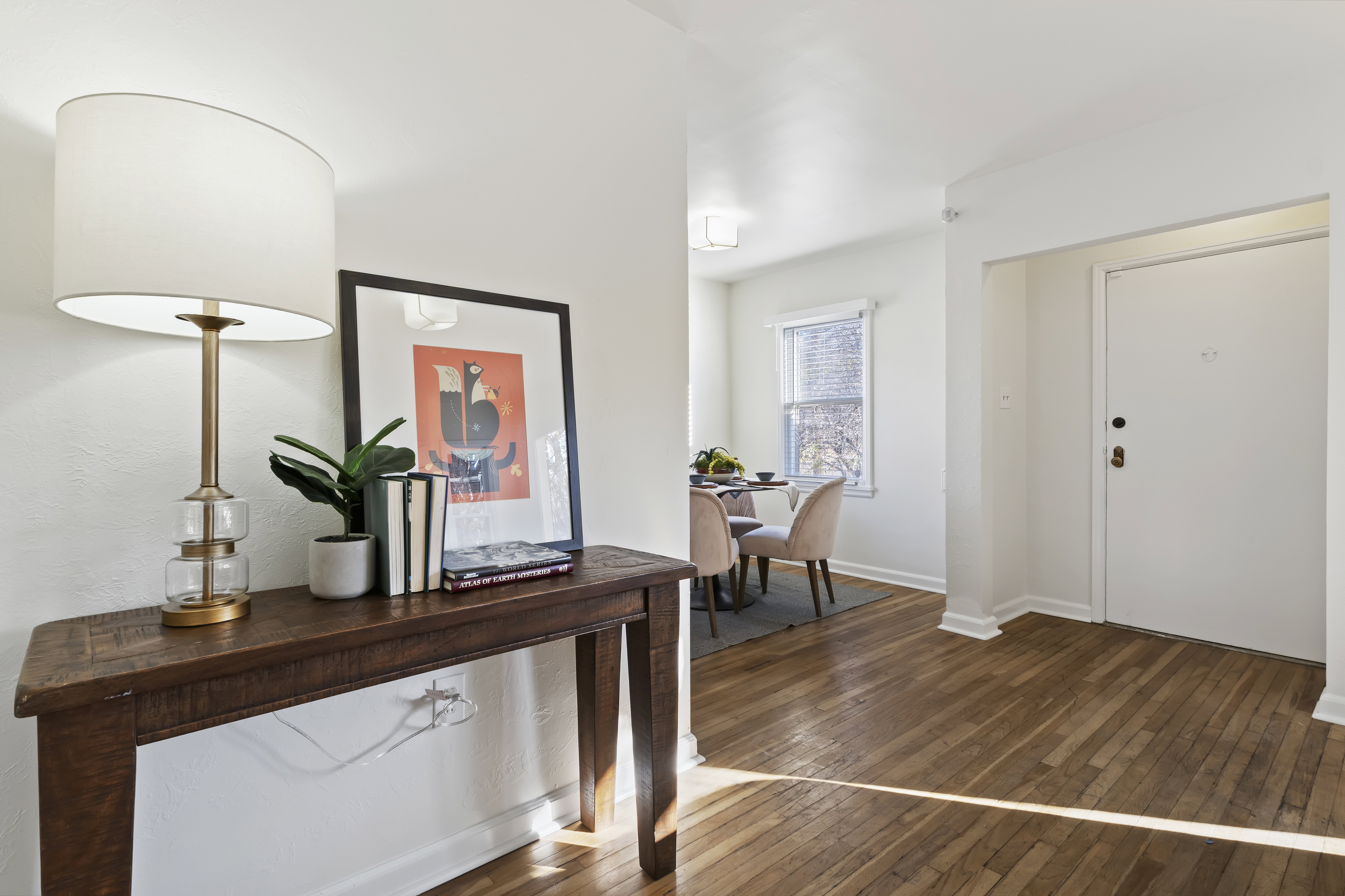 Warm wood-finish flooring extends through the entry and into a dining area featuring a window with blinds