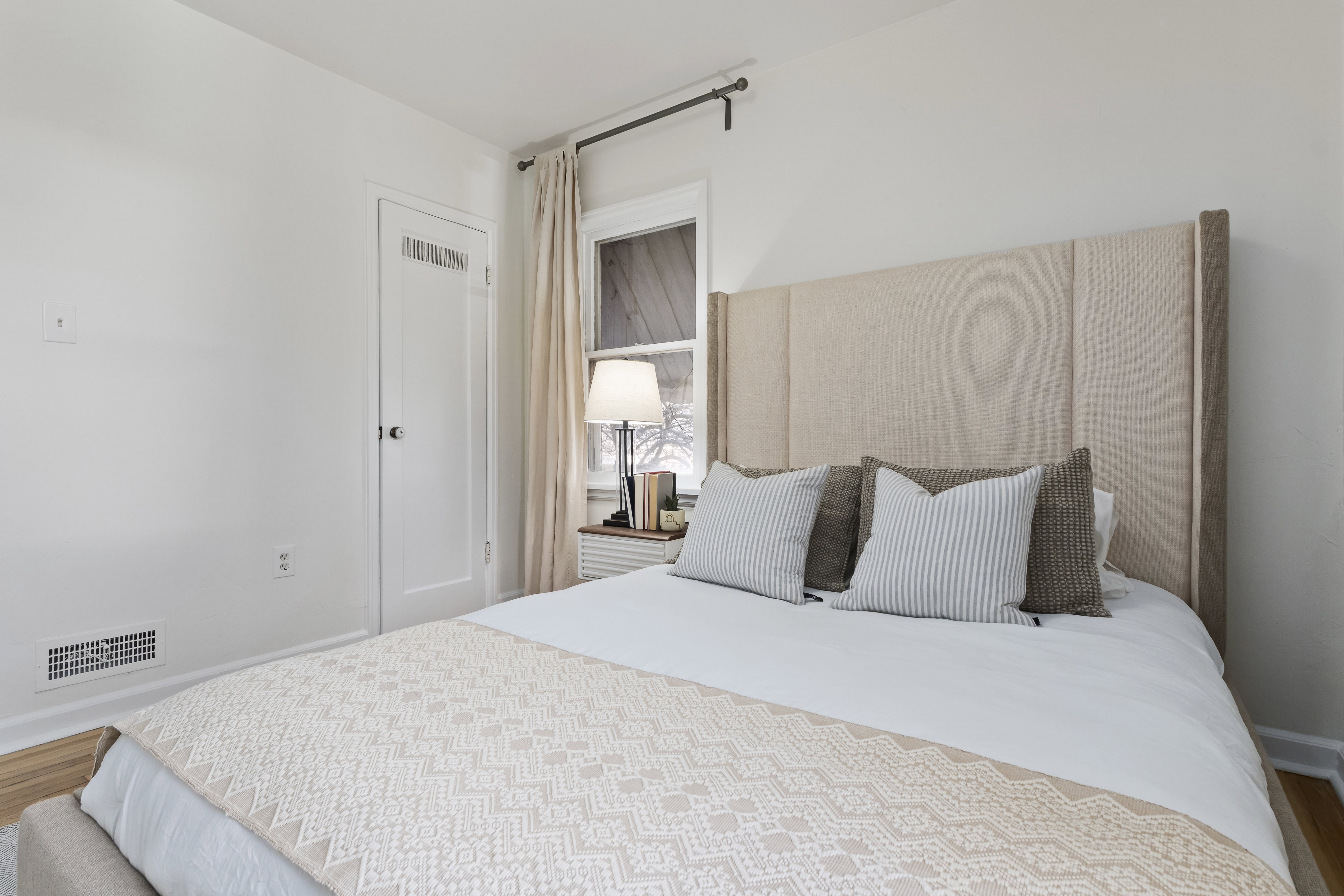 Interior room with white walls, wood-finish flooring, a white louvered door, and a window with light-colored drapes