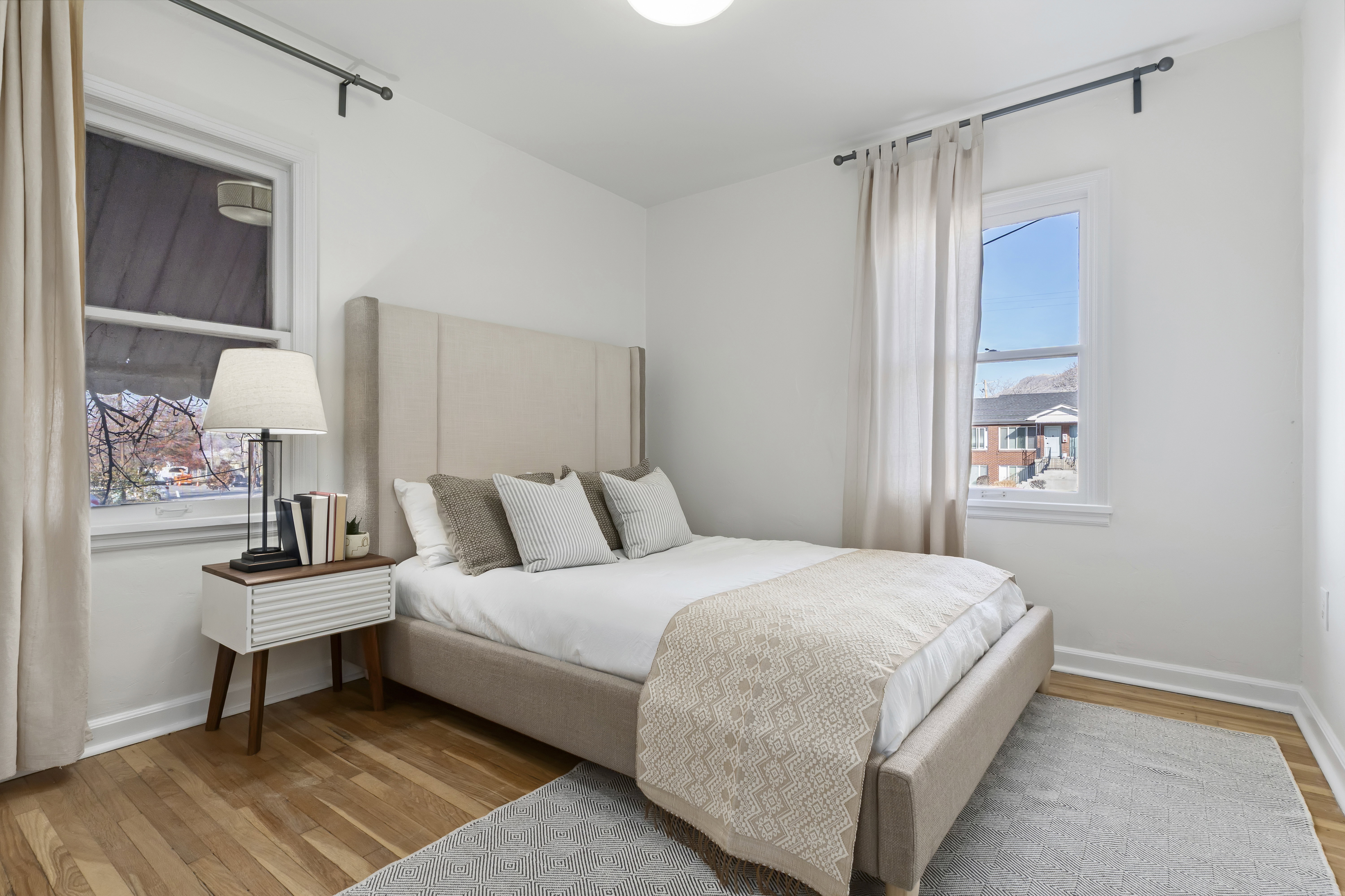 Bedroom featuring wood-finish flooring, white walls, and two windows with black curtain rods