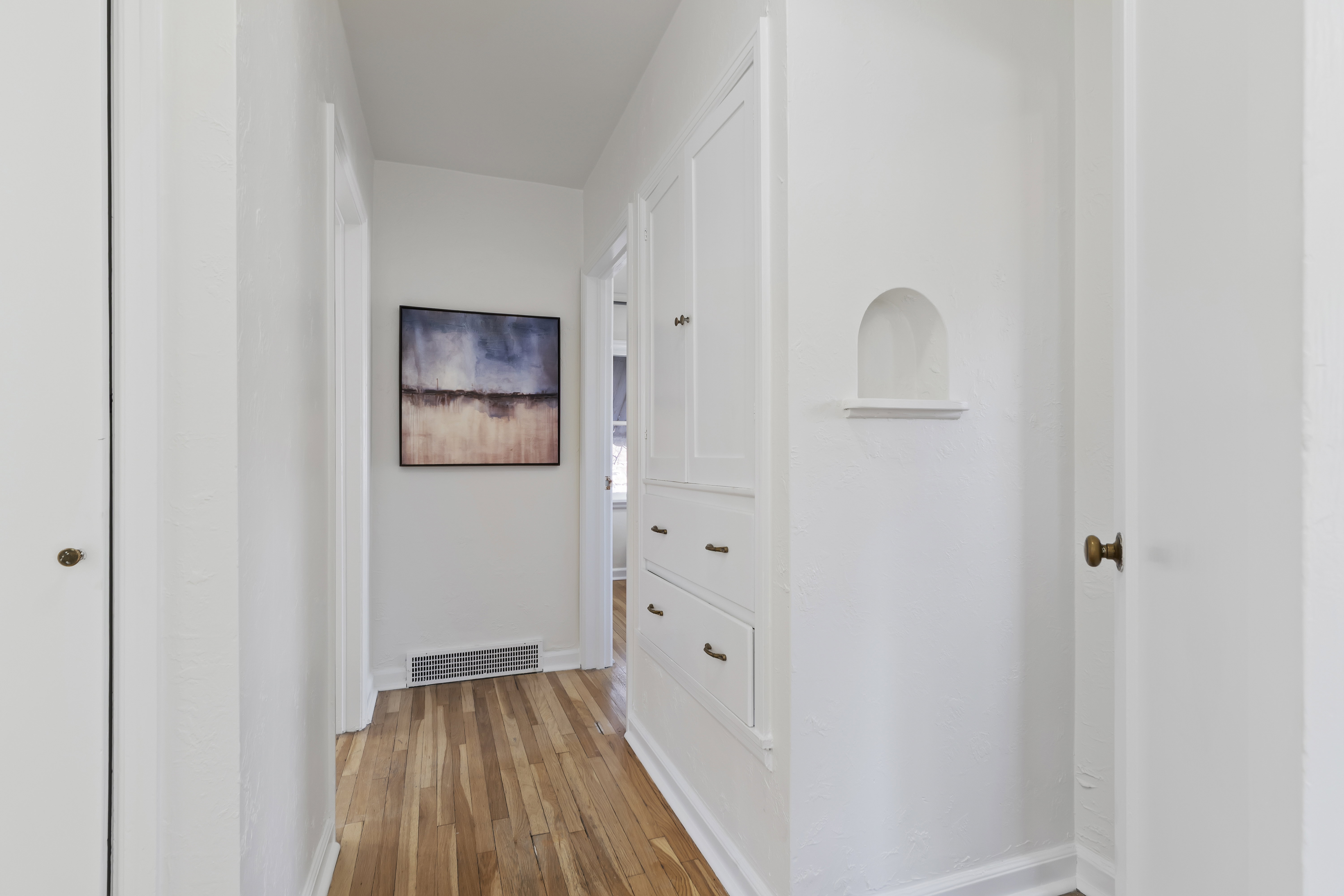 Hallway featuring wood-finish flooring, built-in cabinetry with brass hardware, a recessed wall niche, and white trim