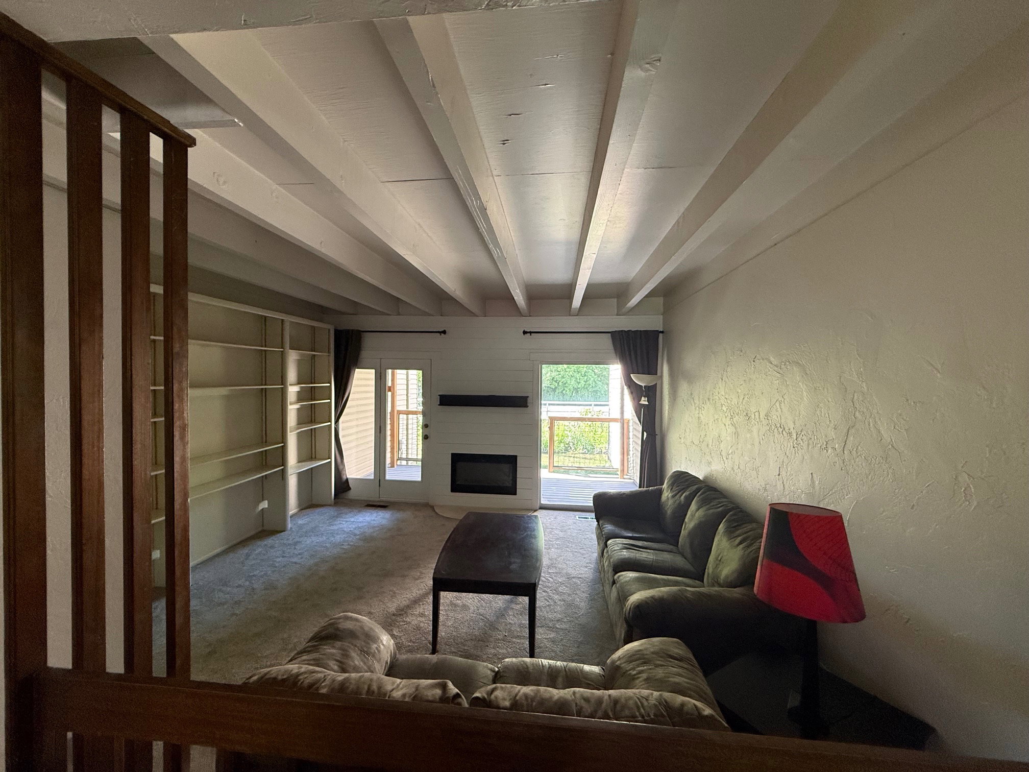 Living area featuring exposed beam ceiling, built-in shelving, an electric fireplace and deck access.