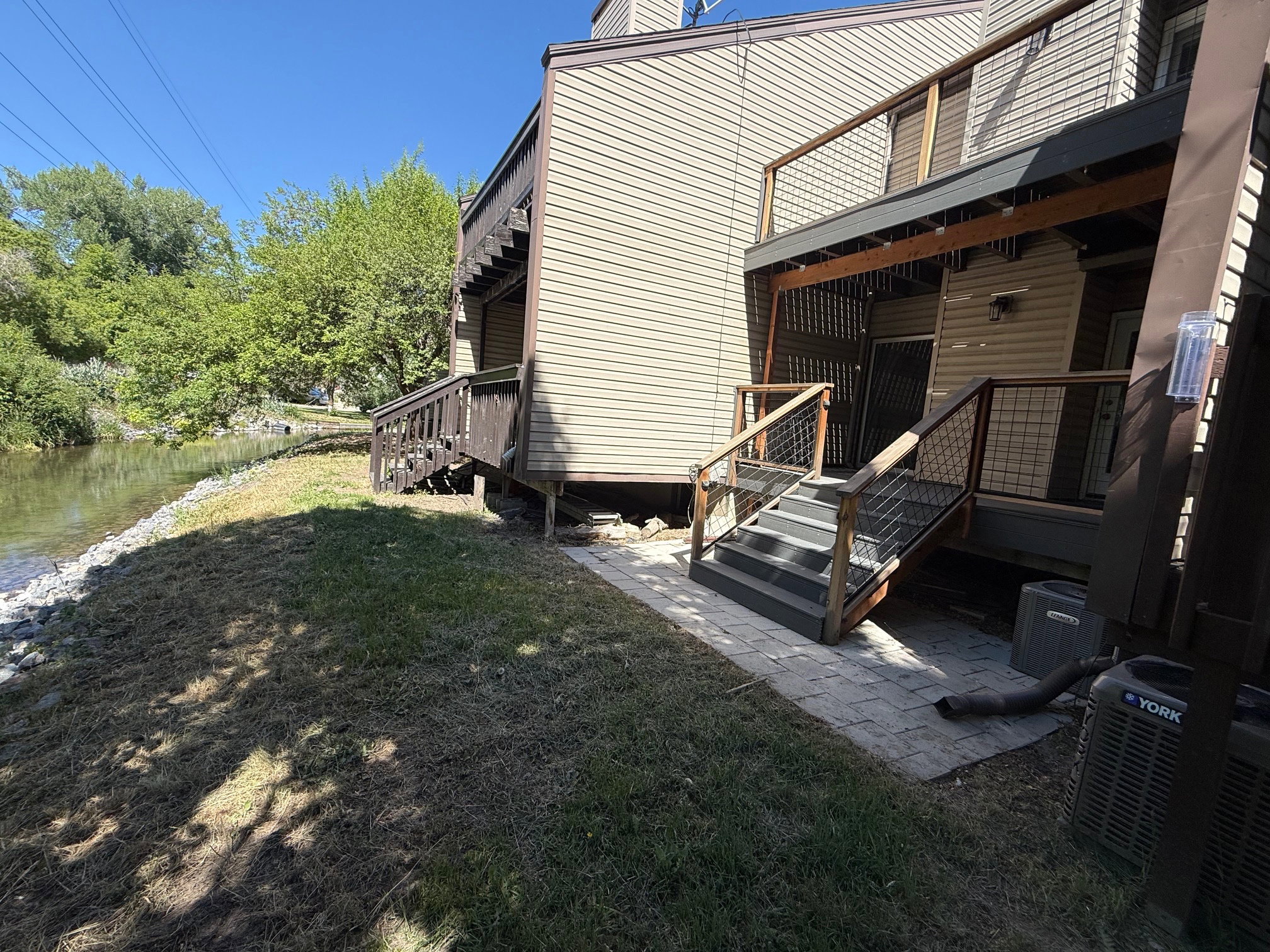 Waterside exterior featuring light-toned siding, a multi-level deck system with wood railing with wire infill, and a lower-level paver patio