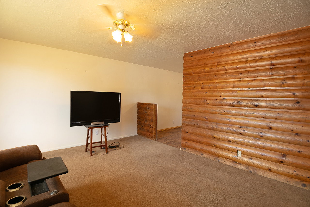 Interior room featuring a prominent log-style accent wall, light-toned carpeting, and a ceiling fan with integrated lighting