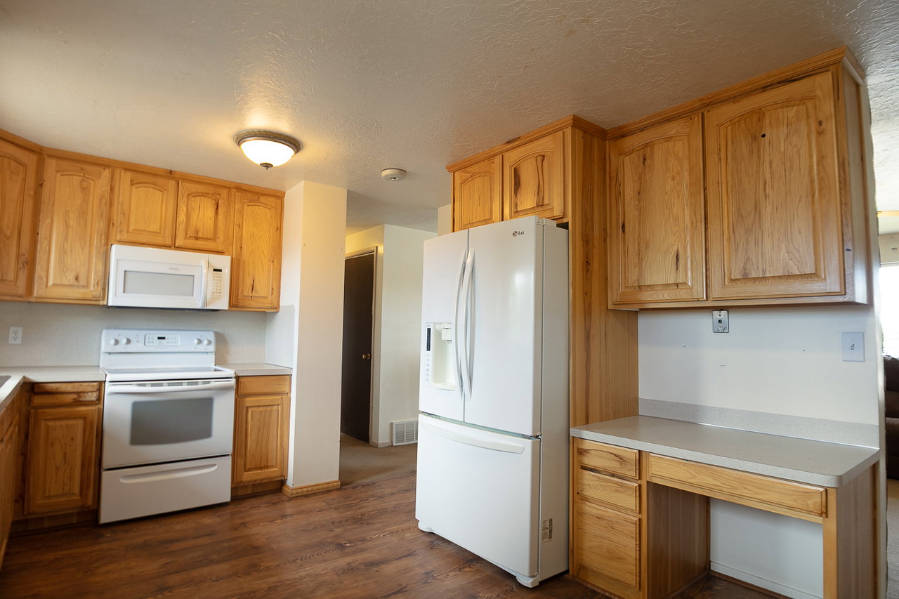 Kitchen featuring wood-finish flooring, light wood cabinetry, white appliances, and a built-in desk area
