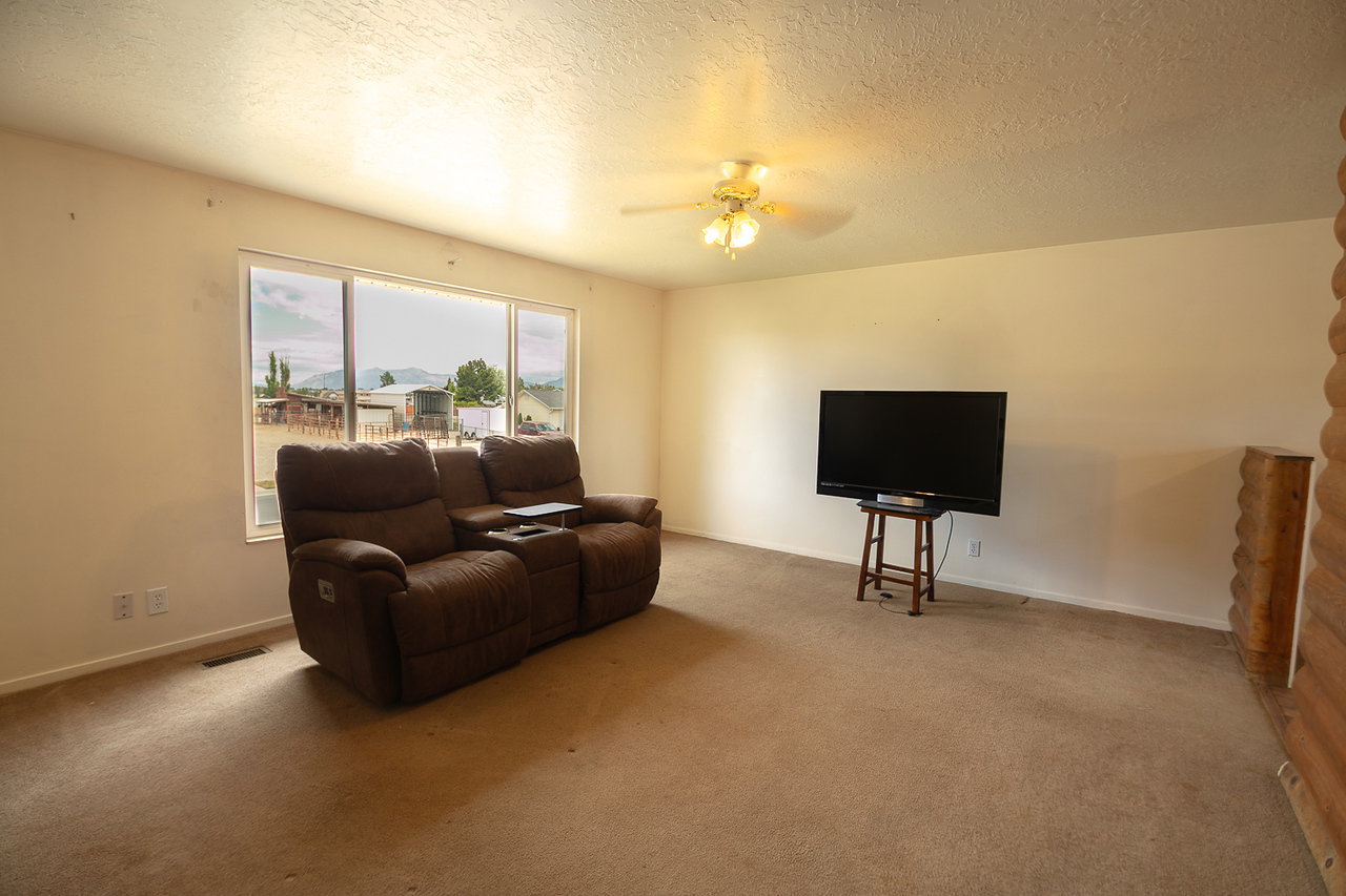 Carpeted interior space featuring a large picture window, textured ceilings, a ceiling fan with light fixture, and a log-style accent wall