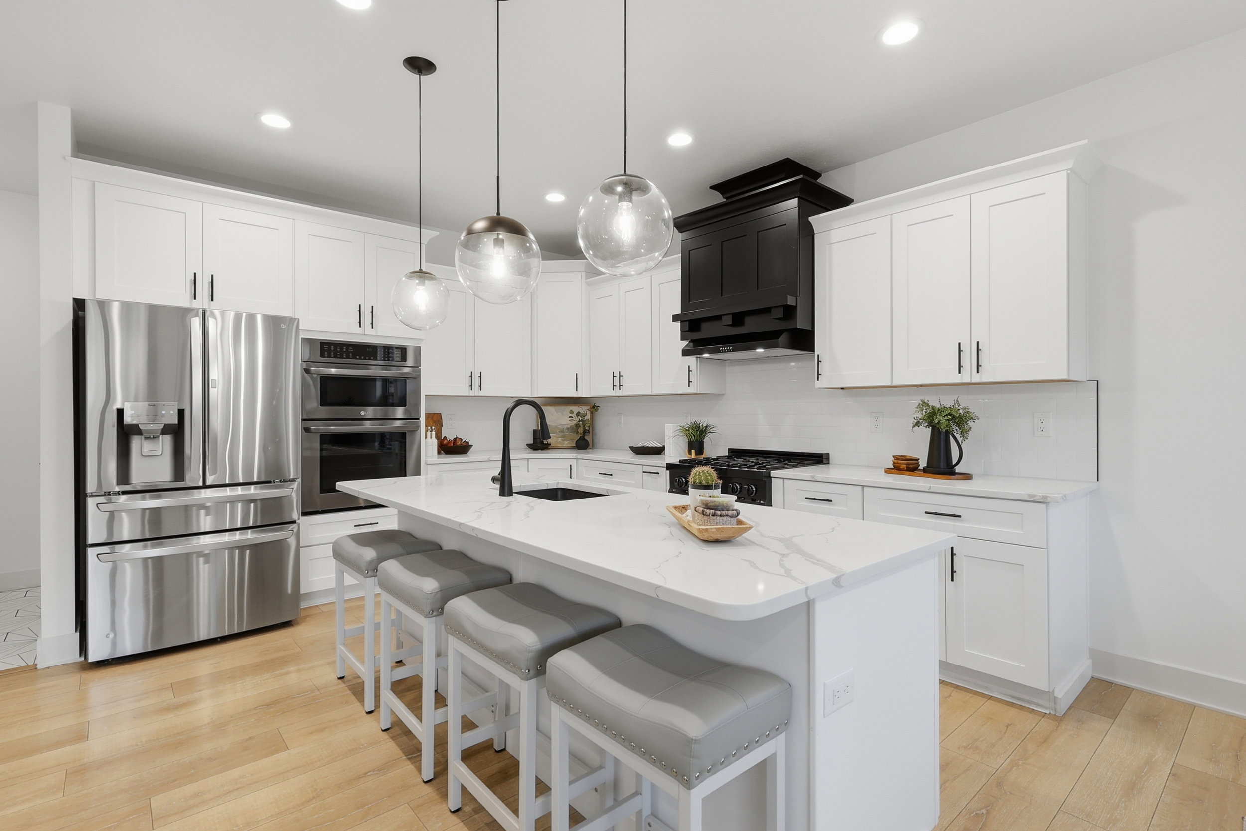 Contemporary kitchen featuring a large central island with seating, white shaker-style cabinetry, and stainless steel appliances, marble countertops