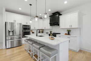 Contemporary kitchen featuring a large central island with seating, white shaker-style cabinetry, and stainless steel appliances, marble countertops