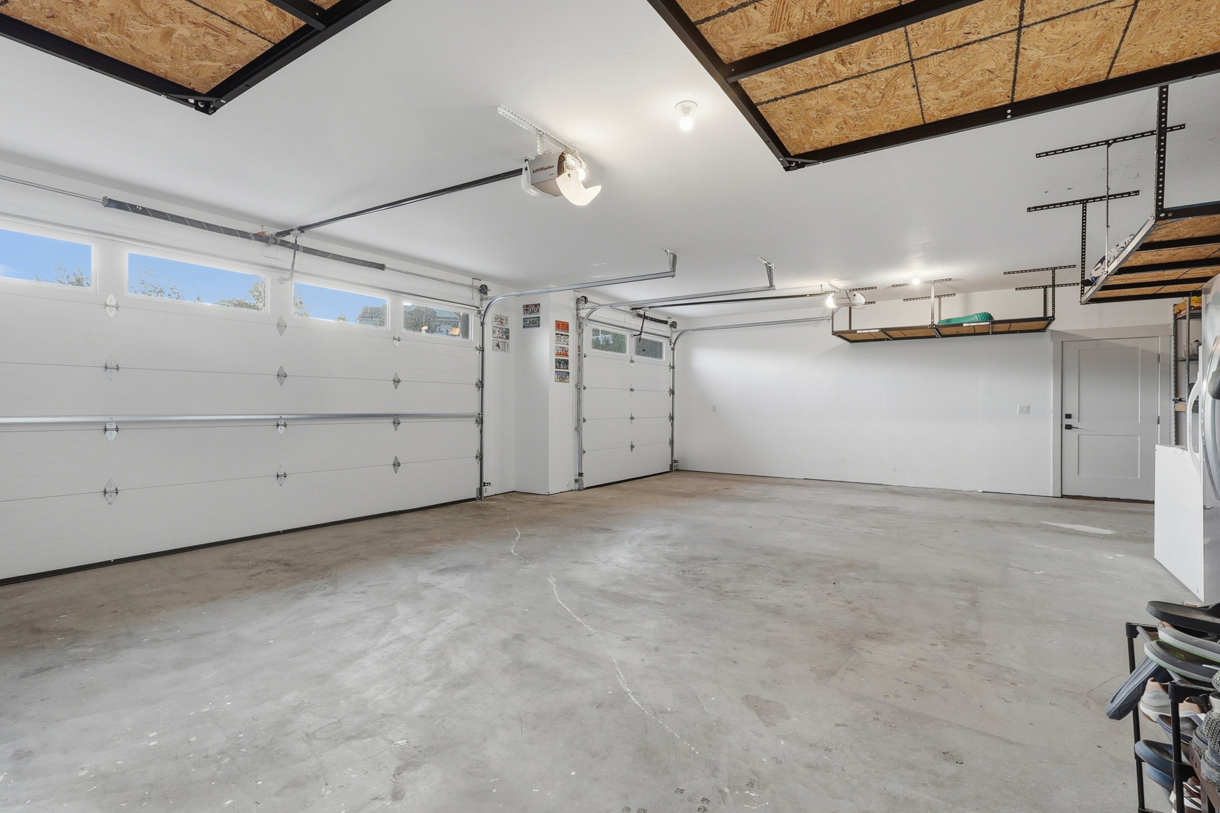 Spacious garage featuring two overhead doors with transom windows, a concrete floor, and ample overhead storage shelving