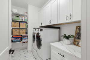 Dedicated laundry space featuring stacked appliances, overhead white shaker cabinetry with black hardware, an integrated counter with a marble-finish surface, and a built-in shelving unit