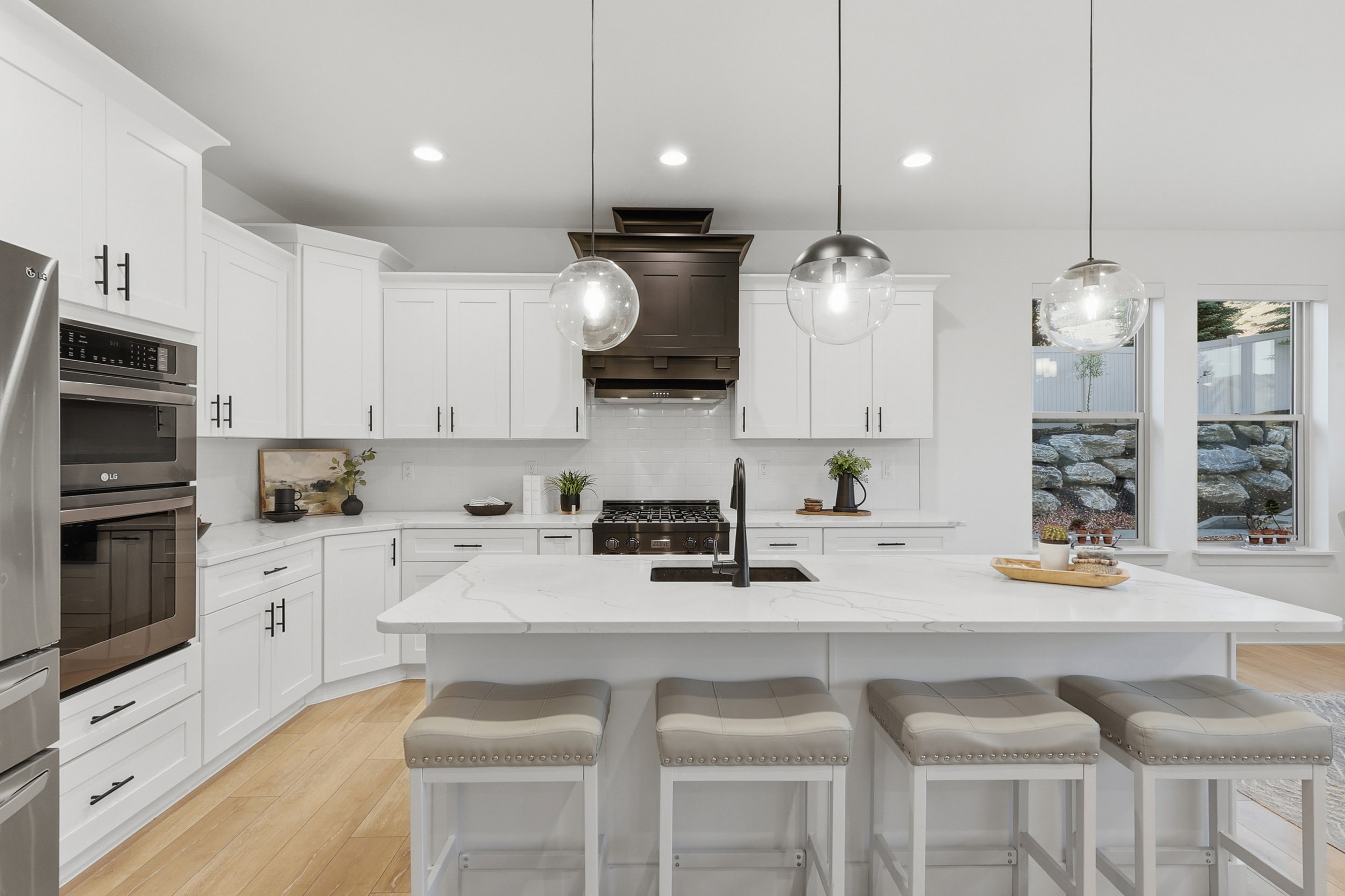 Modern kitchen featuring a large central island with seating, white shaker cabinetry, stainless steel appliances, and wood-finish flooring