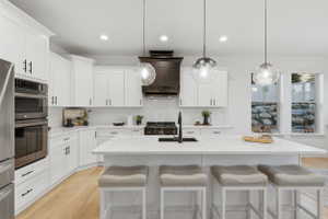 Modern kitchen featuring a large central island with seating, white shaker cabinetry, stainless steel appliances, and wood-finish flooring