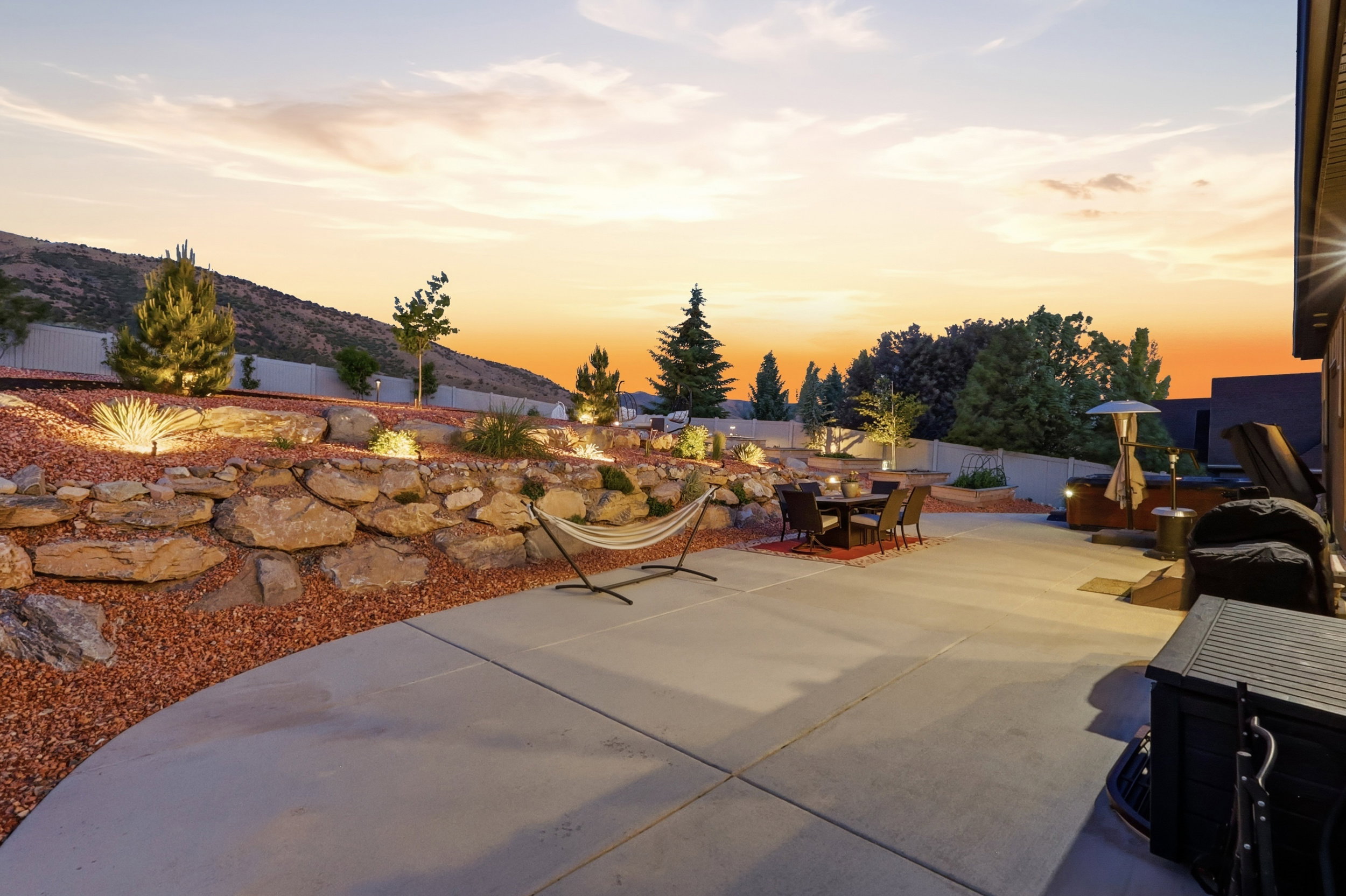 Expansive concrete patio with a tiered rock retaining wall and integrated landscape lighting