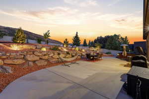 Expansive concrete patio with a tiered rock retaining wall and integrated landscape lighting