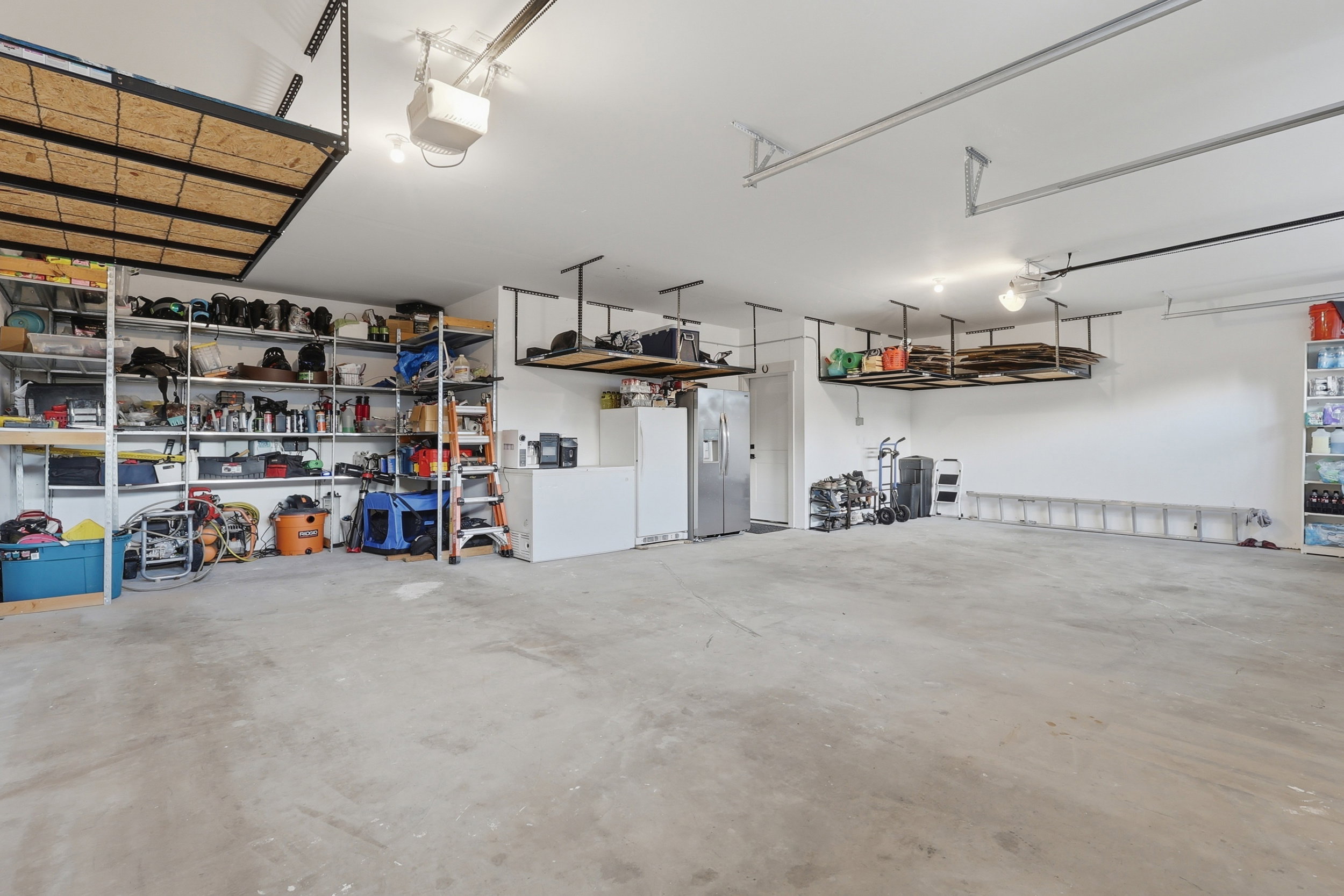 Spacious garage with concrete flooring, overhead storage racks, integrated shelving, and ceiling-mounted lighting