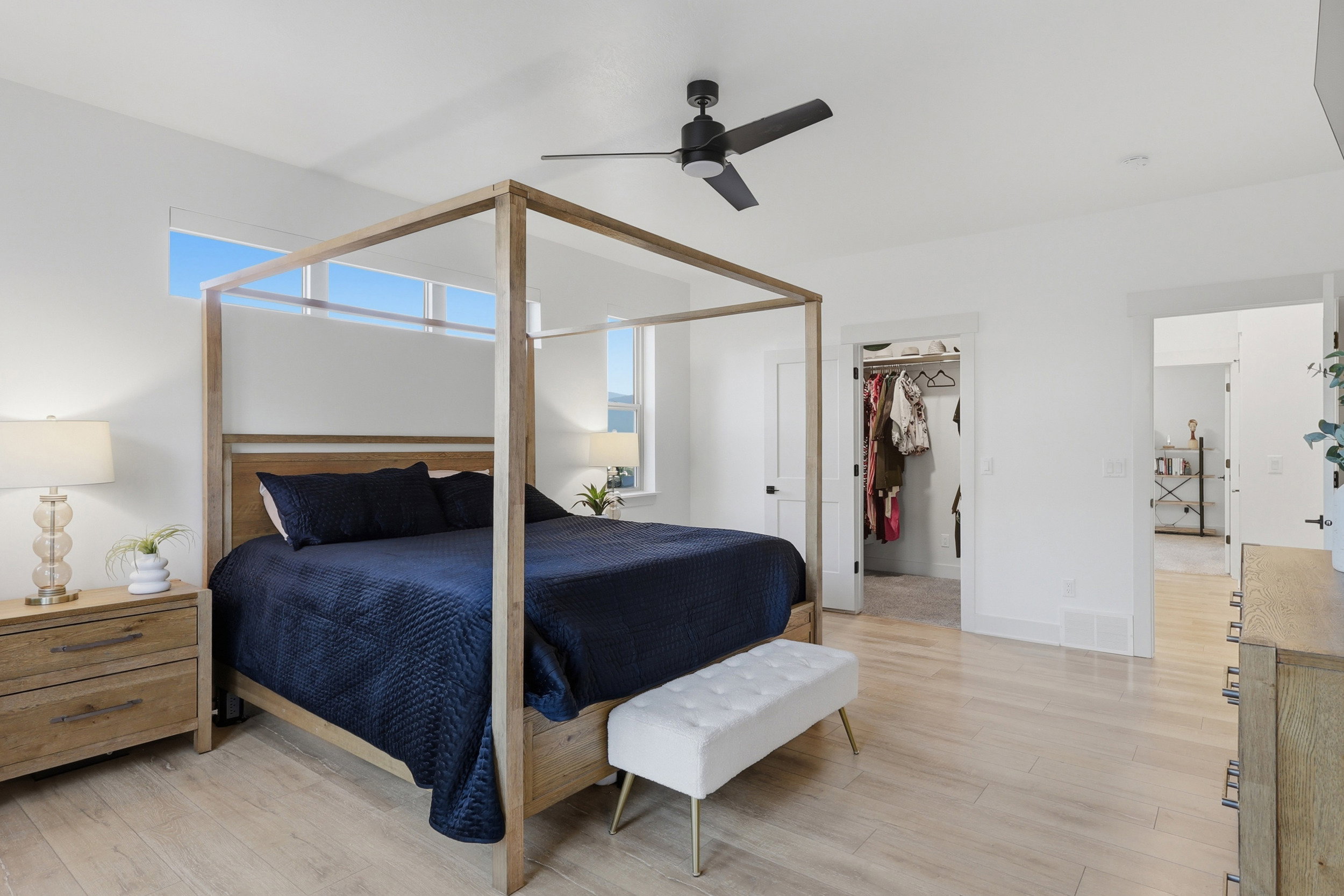 Spacious primary bedroom featuring light wood-finish flooring, a ceiling fan, transom windows, and a walk-in closet