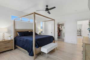 Spacious primary bedroom featuring light wood-finish flooring, a ceiling fan, transom windows, and a walk-in closet