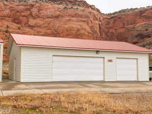 Detached multi-bay garage structure featuring a red corrugated metal roof, white horizontal siding, and multiple white garage doors