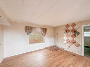 Spacious room featuring wood-finish flooring, a large window, painted white brick wall, and a raised brick hearth