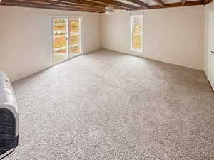 Spacious room featuring exposed ceiling beams, light-colored carpeting, and a ceiling fan