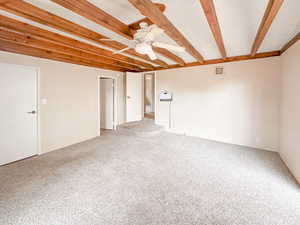 Carpeted room featuring exposed wood beam ceiling, ceiling fan with light fixture, neutral wall paint, and multiple doorways