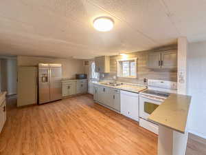 Spacious kitchen featuring wood-finish flooring, light-toned cabinetry, light-colored countertops, a tile backsplash, and a built-in breakfast bar