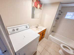 Compact bathroom featuring a built-in tub with shower, a vanity with a countertop sink, a wall-mounted mirror, and tile flooring
