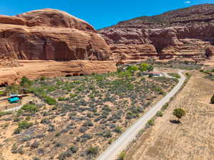 Expansive desert landscape featuring natural rock formations, a winding unpaved road, and distant residential structures