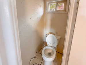 Compact water closet featuring a standard toilet, square tiled flooring, and a single-pane window