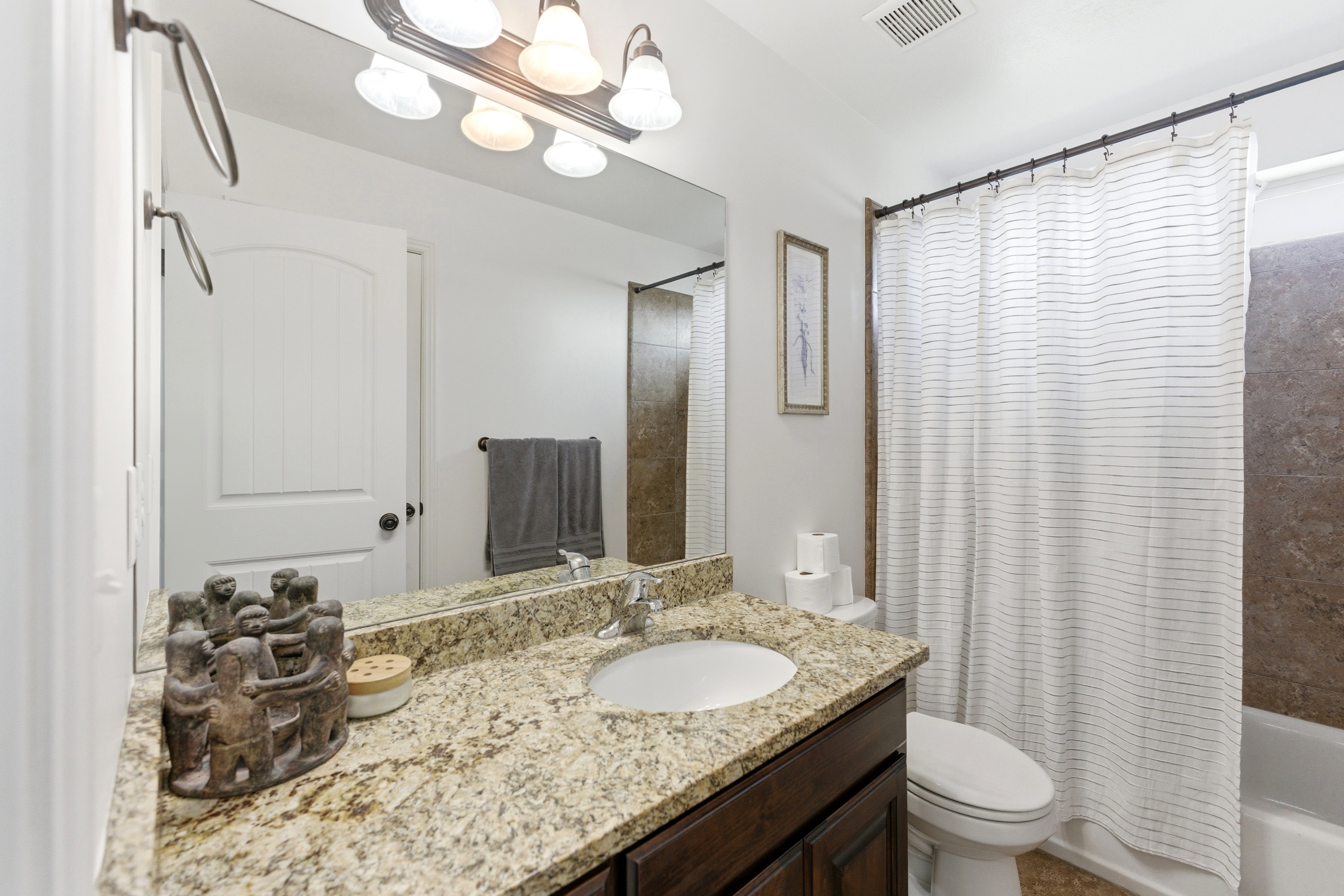 Bathroom featuring a single vanity with a granite countertop, undermount sink, and dark wood cabinetry