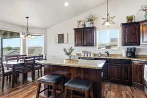 Open-concept kitchen featuring wood-finish flooring, dark wood cabinetry, and granite countertops