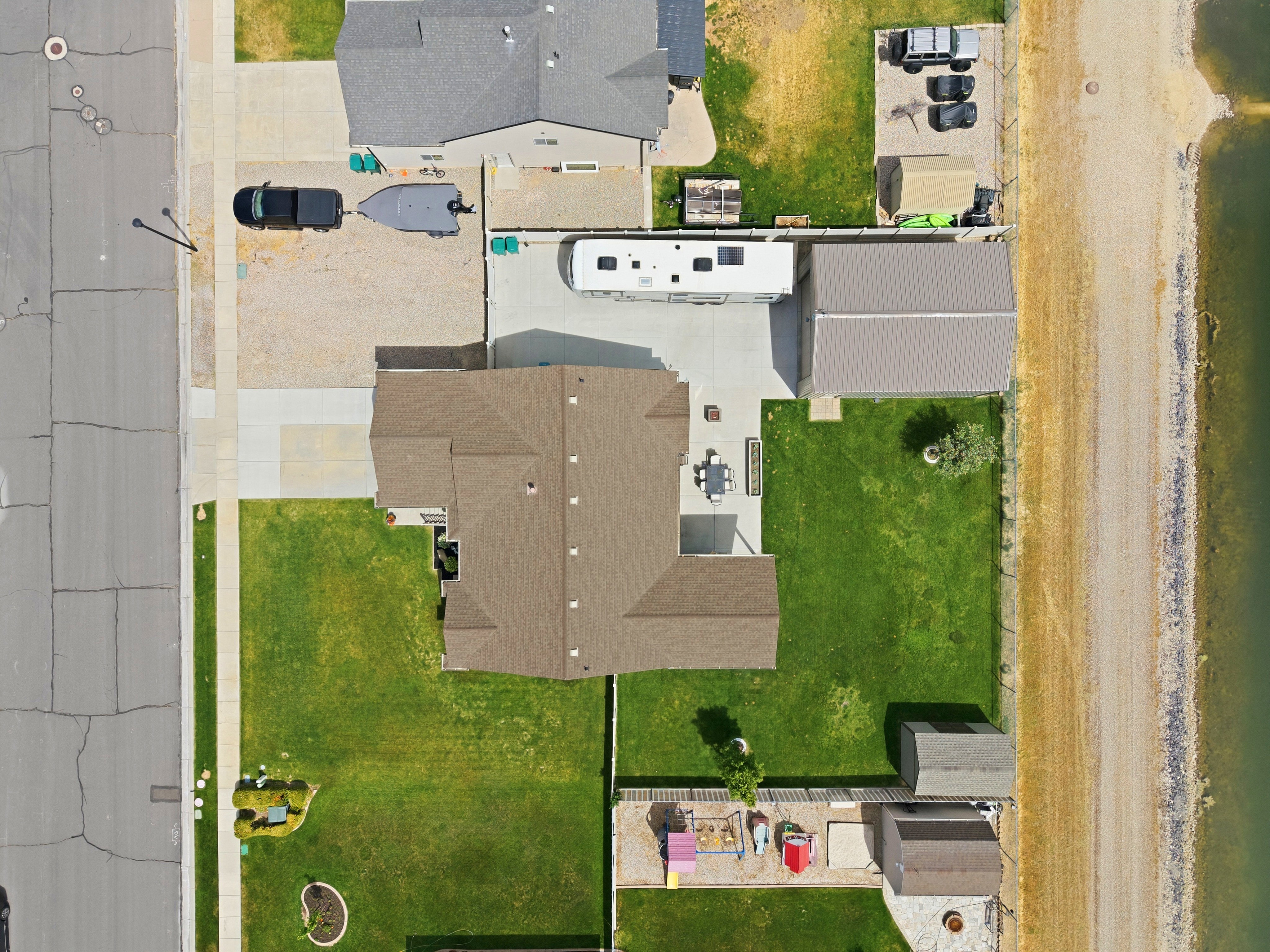 Expansive property featuring a large main residence with a brown shingle roof, a generously sized green lawn, shop and a paved patio area