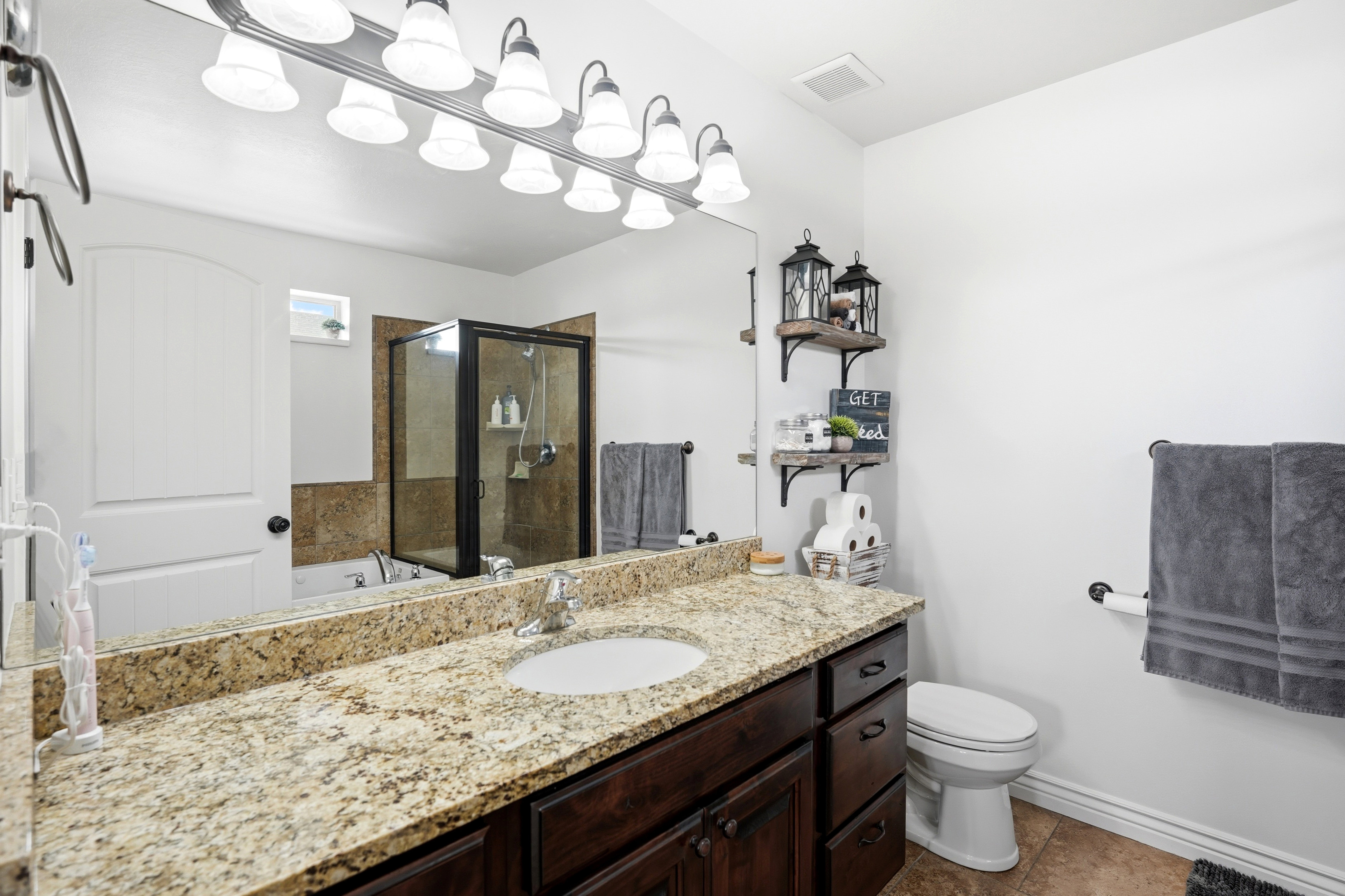 Master bathroom featuring a granite-look countertop with an under-mount sink, a dark wood-finish vanity, and a large mirror with multi-bulb lighting