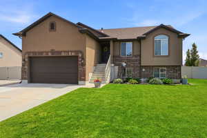Stucco and brick facade residence featuring a two-car garage, concrete driveway, and front lawn