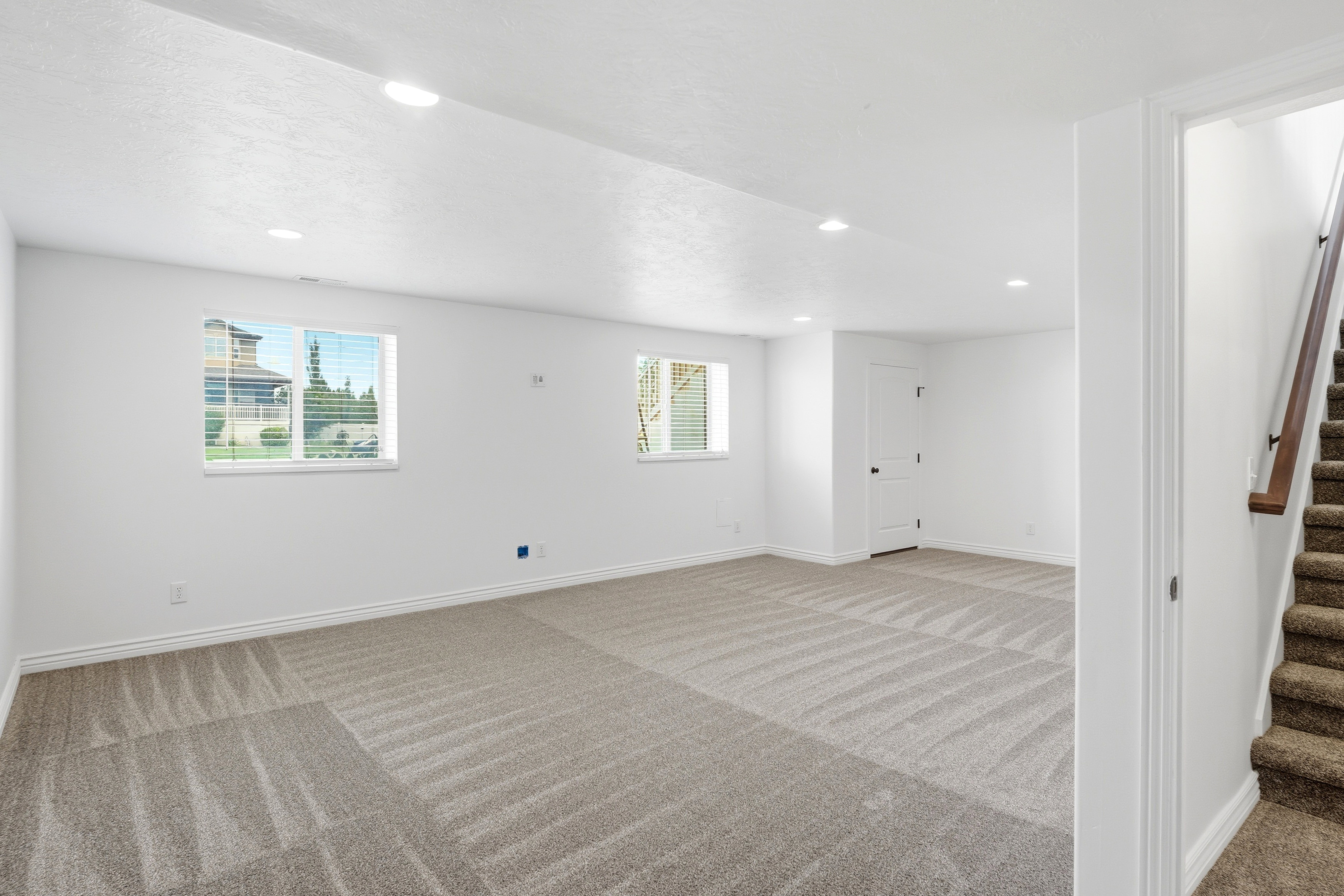 Spacious lower-level bedroom featuring carpet flooring, recessed lighting, and two windows with blinds