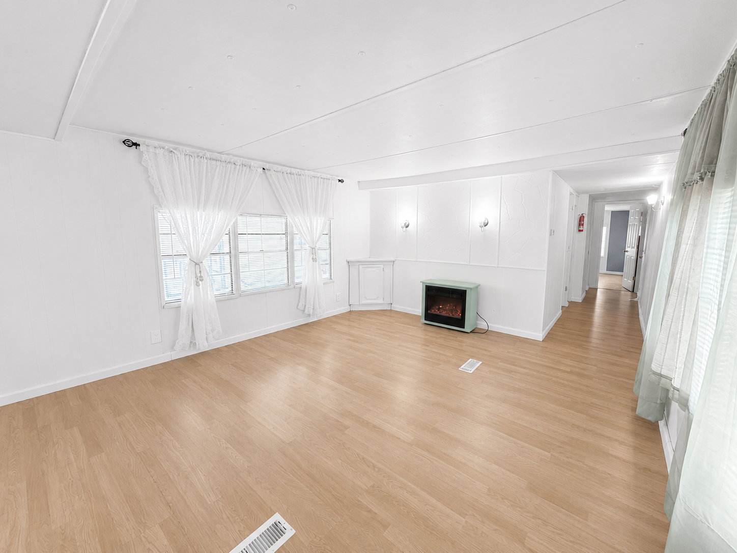 Bright and open living room featuring light flooring, white walls, large windows, and an electric fireplace.