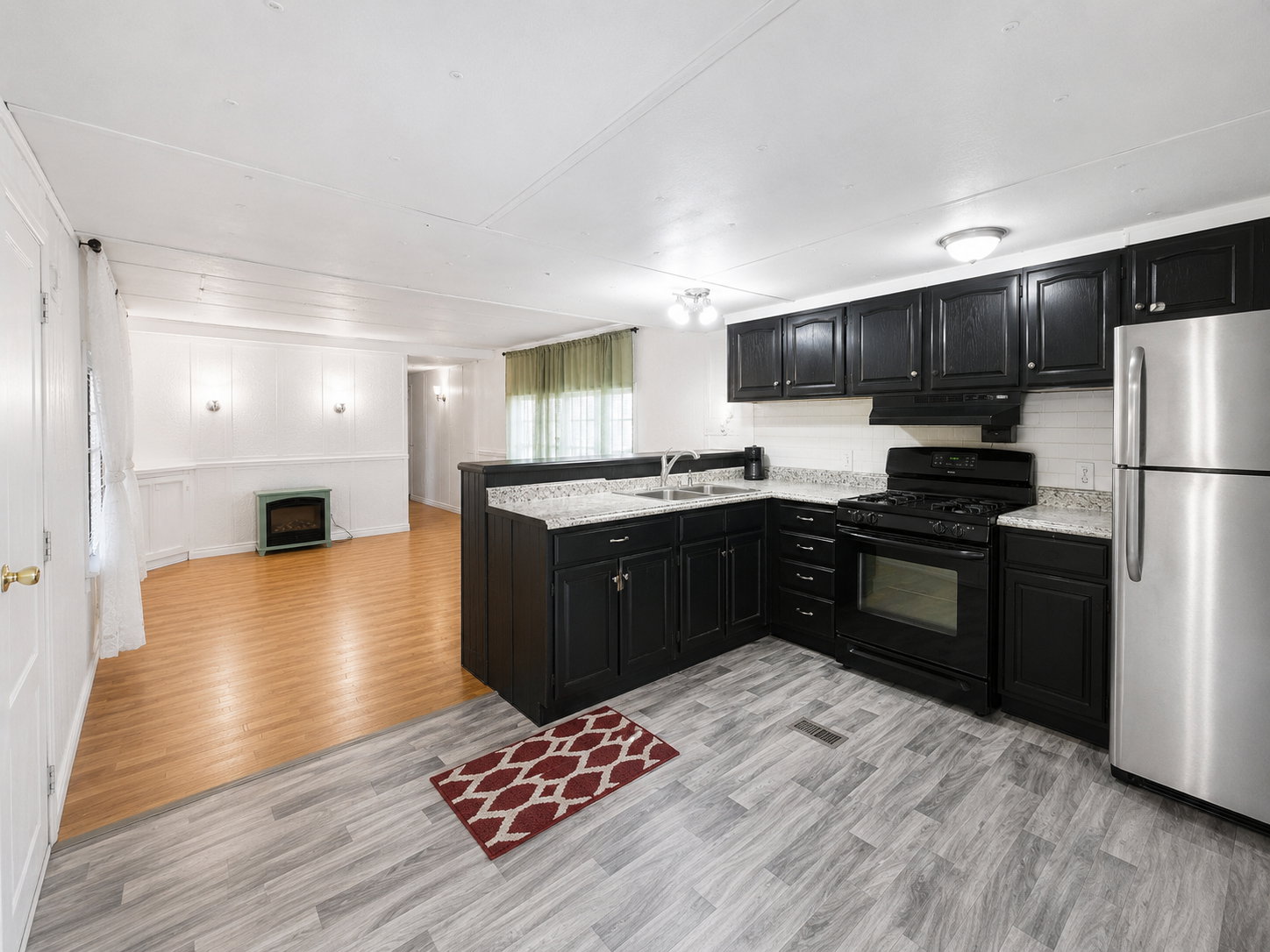 Open kitchen and living area featuring black cabinetry, stainless steel appliances, light countertops, and easy flow into the main living space.
