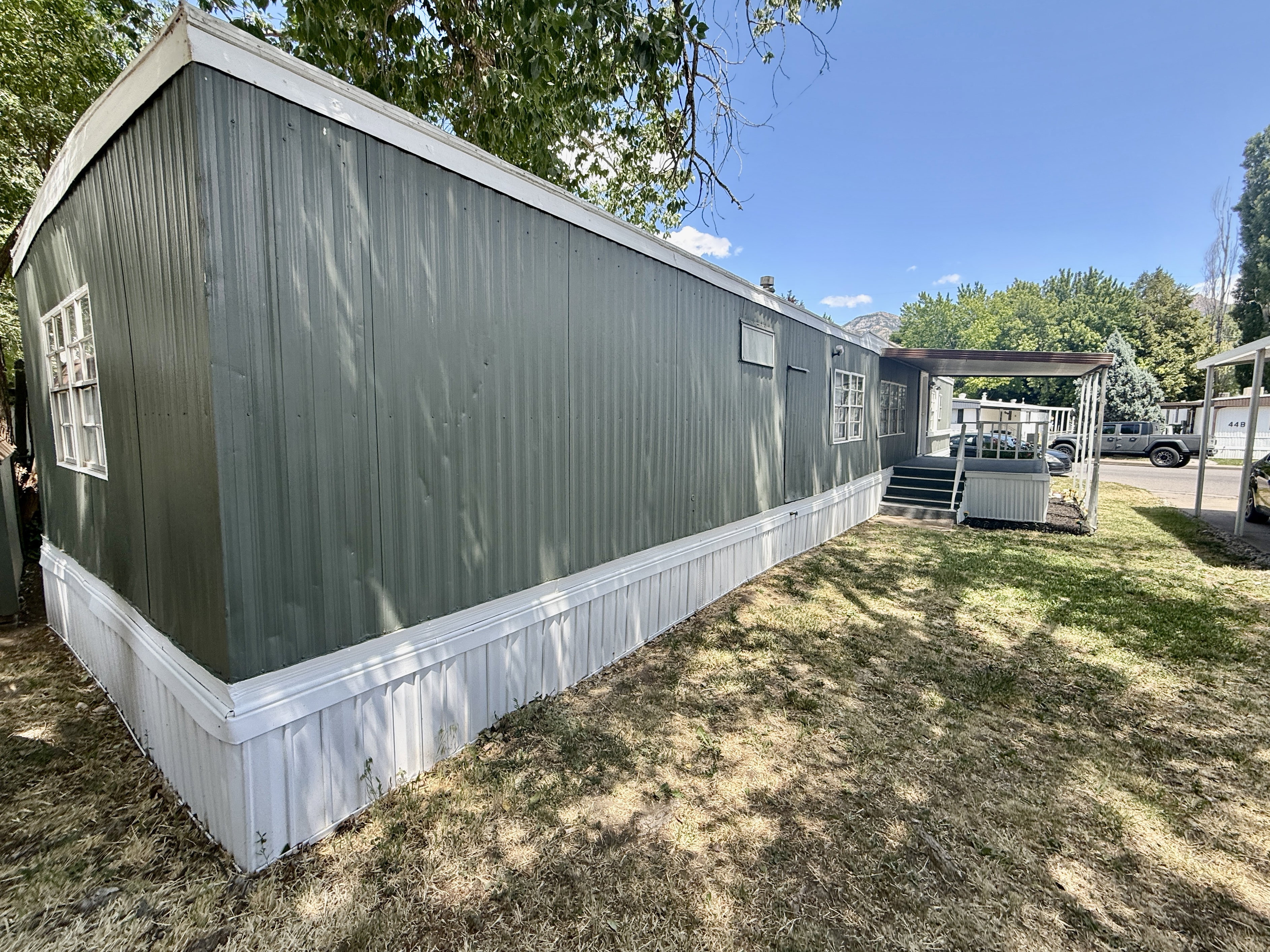 Back side exterior view featuring mature shade trees, lawn area, and easy access to the covered entry.