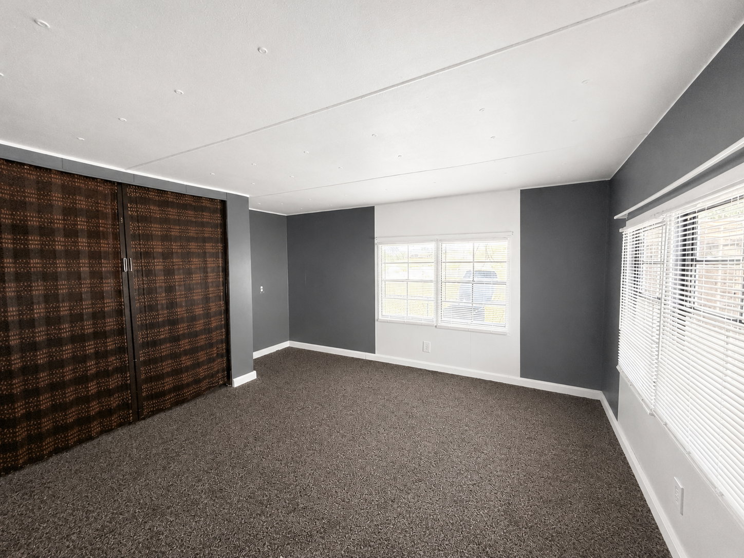 Large bedroom with dark carpet, gray accent walls, multiple windows, and generous closet space.